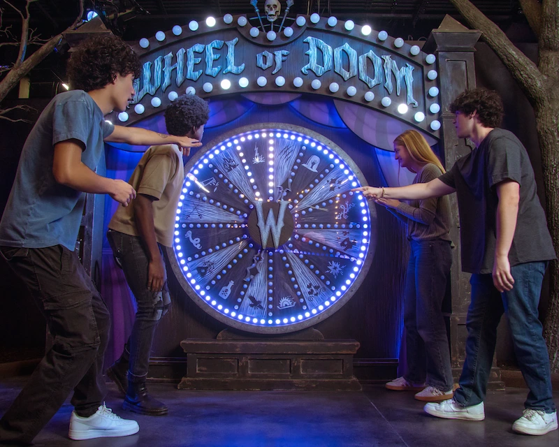 Friends gather around a "Wheel of Doom" carnival game.