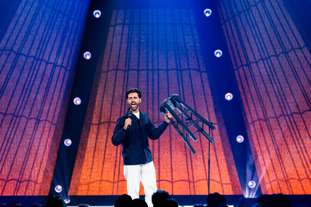 Hasan Minhaj holding up a stool during his stand-up special.