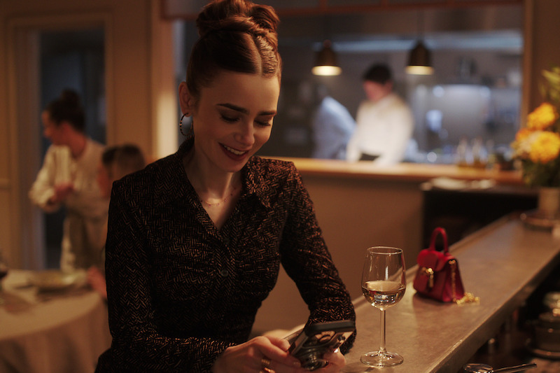 Lily Collins, como Emily, sorri em um bar na temporada 4 de ‘Emily em Paris’