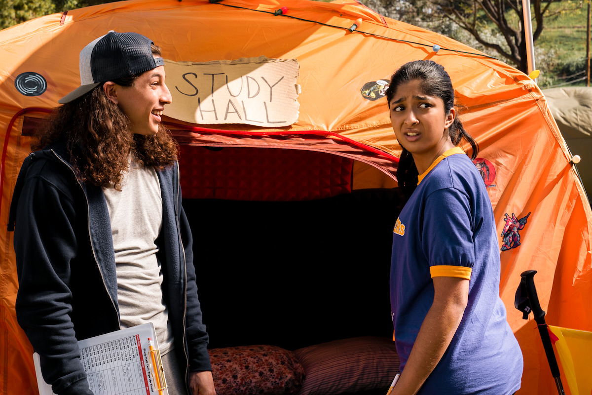 Benjamin Norris as Trent Harrison and Maitreyi Ramakrishnan as Devi Vishwakumar stand in front of an orange tent in ‘Never Have I Ever’ Season 2.