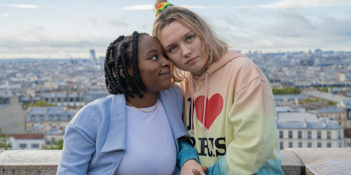 Corinna Brown as Tara and Kizzy Edgell as Darcy stand together with the cityscape of Paris behind them in Season 2 of ‘Heartstopper.’
