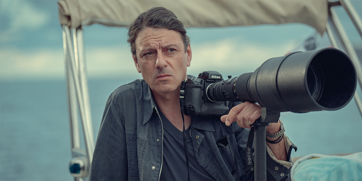 Italian paparazzo Mario Brenna (Enzo Cilenti) holding a camera with a telephoto lens