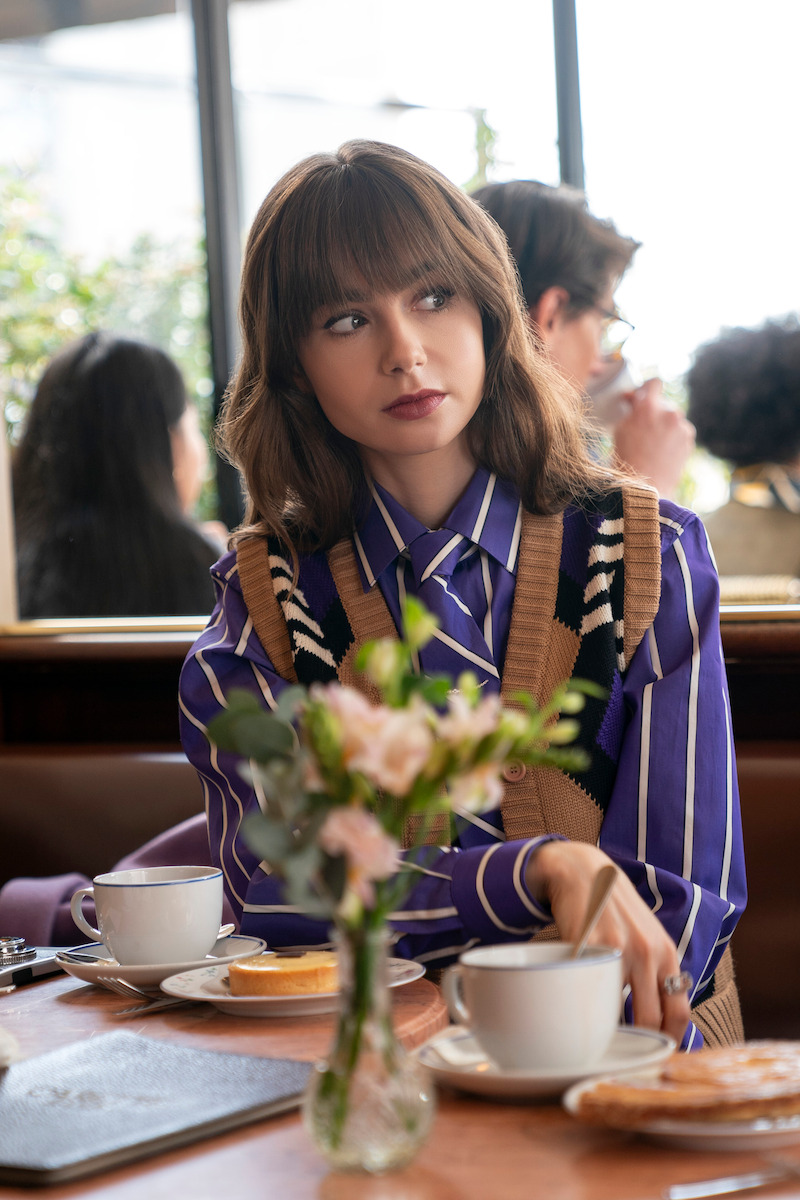 Lily Collins, como Emily, sentada em uma cafeteria na temporada 4 de ‘Emily em Paris’