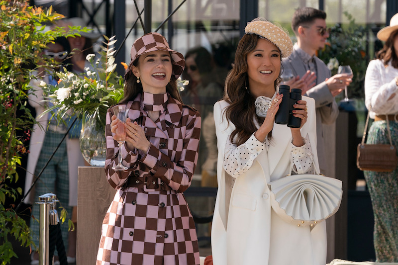 Lily Collins, como Emily, e Ashley Park, como Mindy, caminham lado a lado por uma rua na temporada 4 de ‘Emily em Paris’