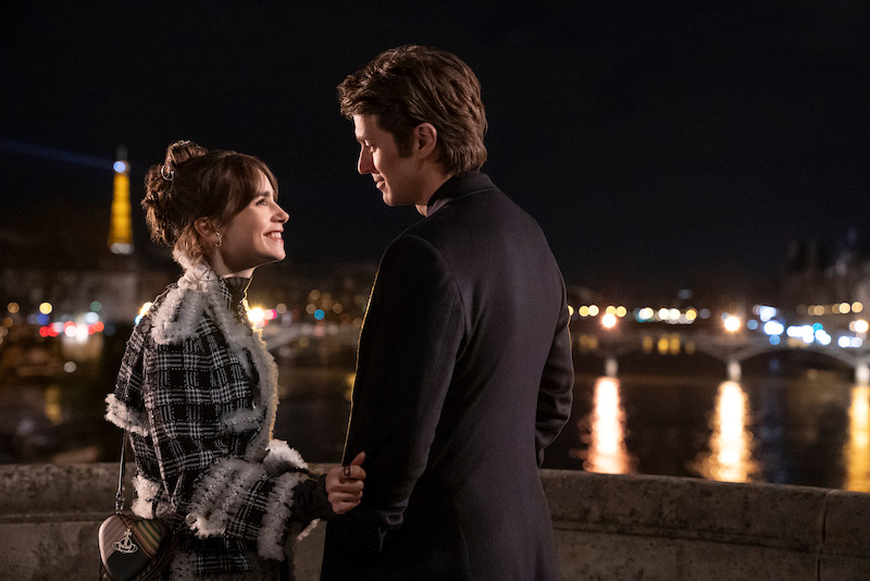 Lily Collins, como Emily, e Lucas Bravo, como Gabriel, sorriem um para o outro em uma ponte na temporada 4 de ‘Emily em Paris’