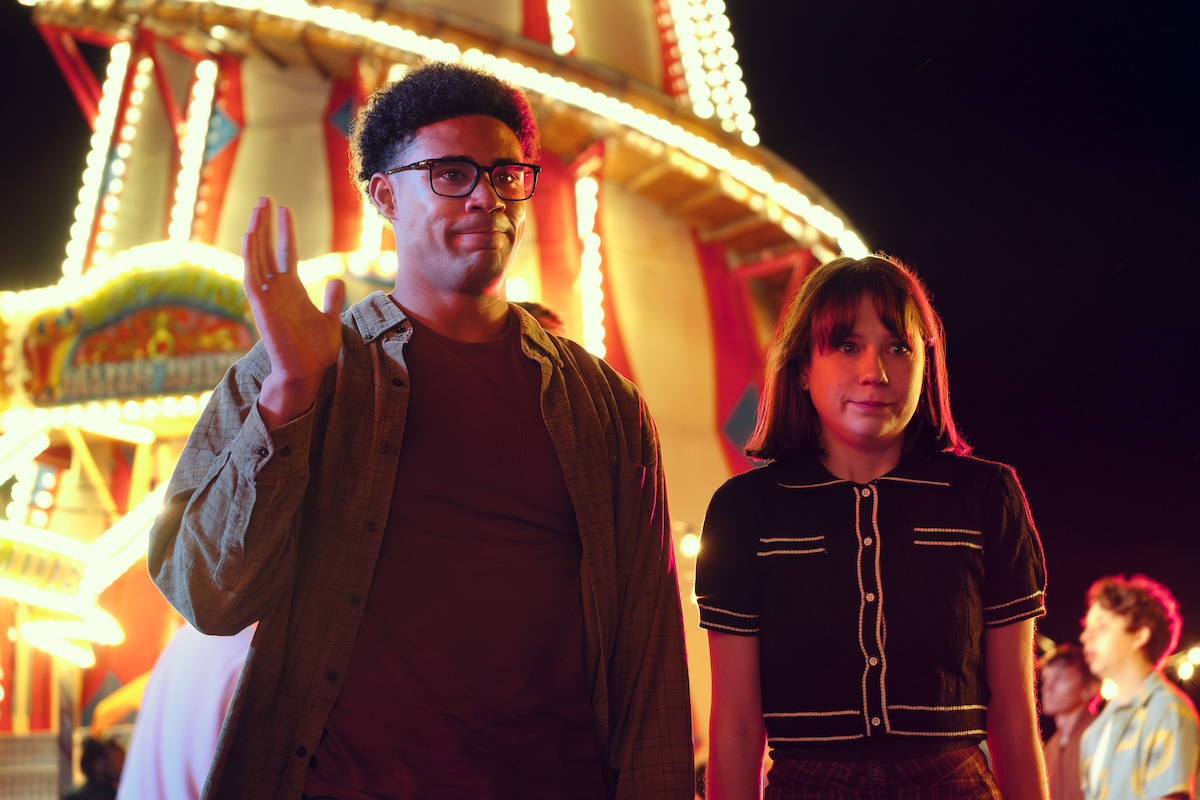 Darragh Hand como Michael e Jenny Walser como Tori juntos em um parque de diversões, com expressões constrangidas, na temporada 3 de ‘Heartstopper’.