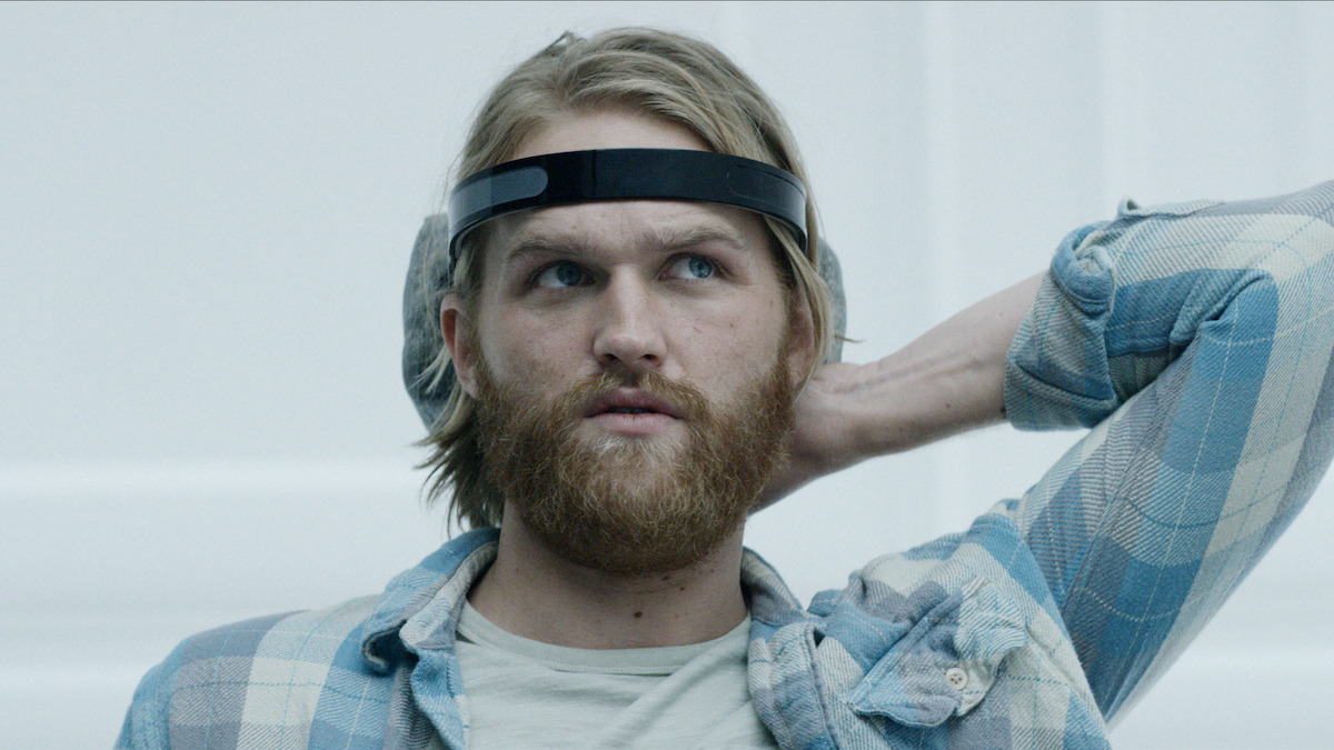 A man with a device on his head sits in a white room in Season 3 of 'Black Mirror'