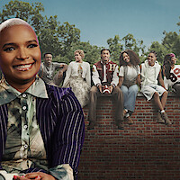 Felicia Pride sorrindo em frente a uma foto do elenco de Um Mundo Diferente