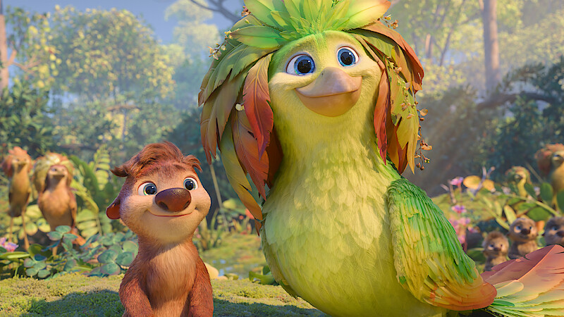 Animated forest scene with a smiling small brown furry creature and a large vibrant green bird with leafy feathers, surrounded by lush greenery, trees, and other animals in the background under daylight.