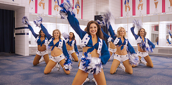 Formation of cheerleaders in DCC uniform practice inside fitting room in triangle formation while raising their right hands with pom poms up in the air confidently.