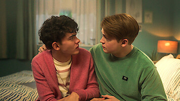 Joe Locke como Charlie e Kit Connor como Nick estão sentados lado a lado na cama e trocando olhares na temporada 3 de ‘Heartstopper’