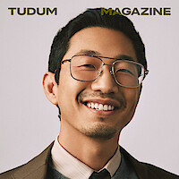 Lee Sung Jin stands in front of a cream backdrop, smiling and looking to camera.