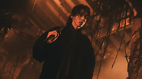 Person in dark clothing holding a weapon, standing in a dimly lit, eerie environment with hanging vines and dramatic orange lighting, evoking a tense, mysterious atmosphere.