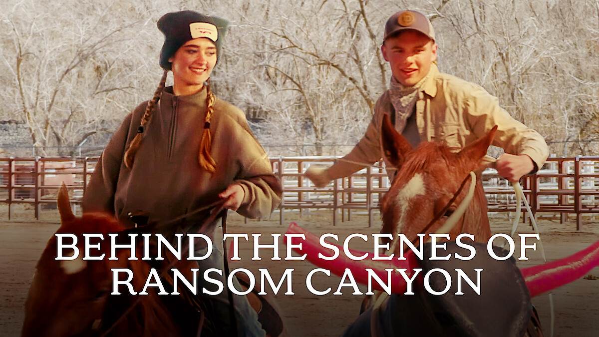 From left to right, Lizzy Greene and Garrett Wareing are smiling while riding horses in a fenced area with bare trees. Text reads "BEHIND THE SCENES OF RANSOM CANYON" at the bottom.